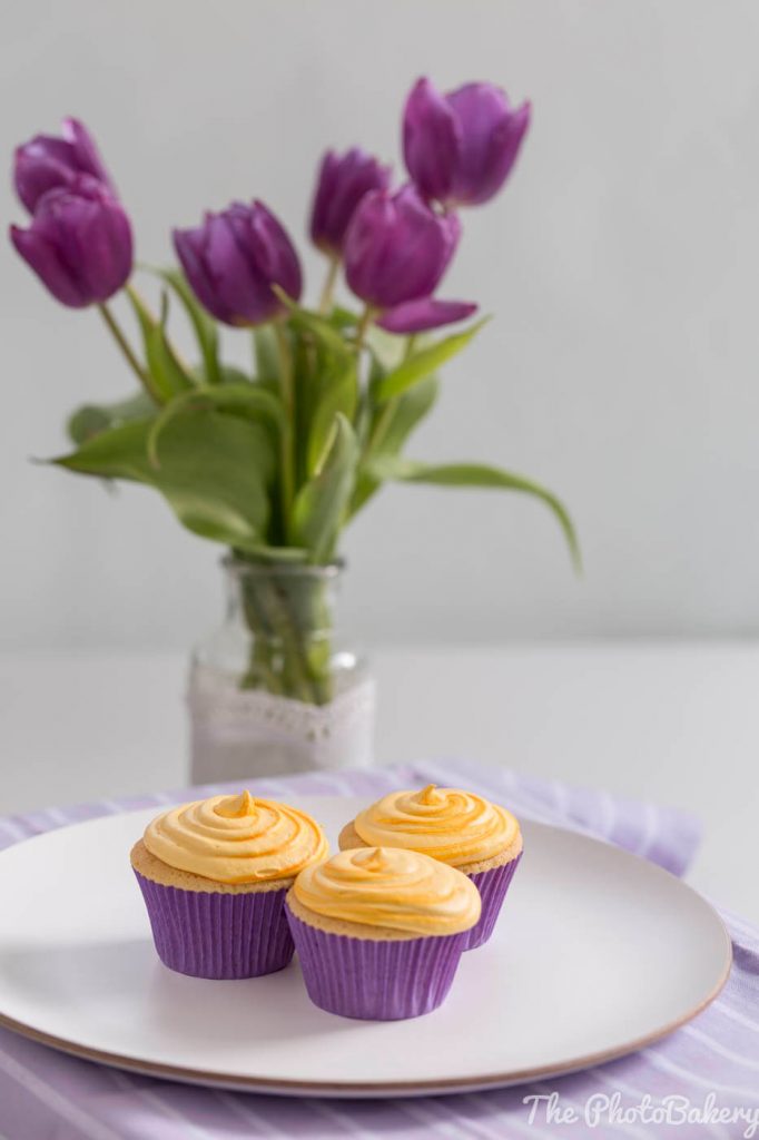 gelbe Zitronen Cupcakes in lila Förmchen mit Tulpen im Hintergrund